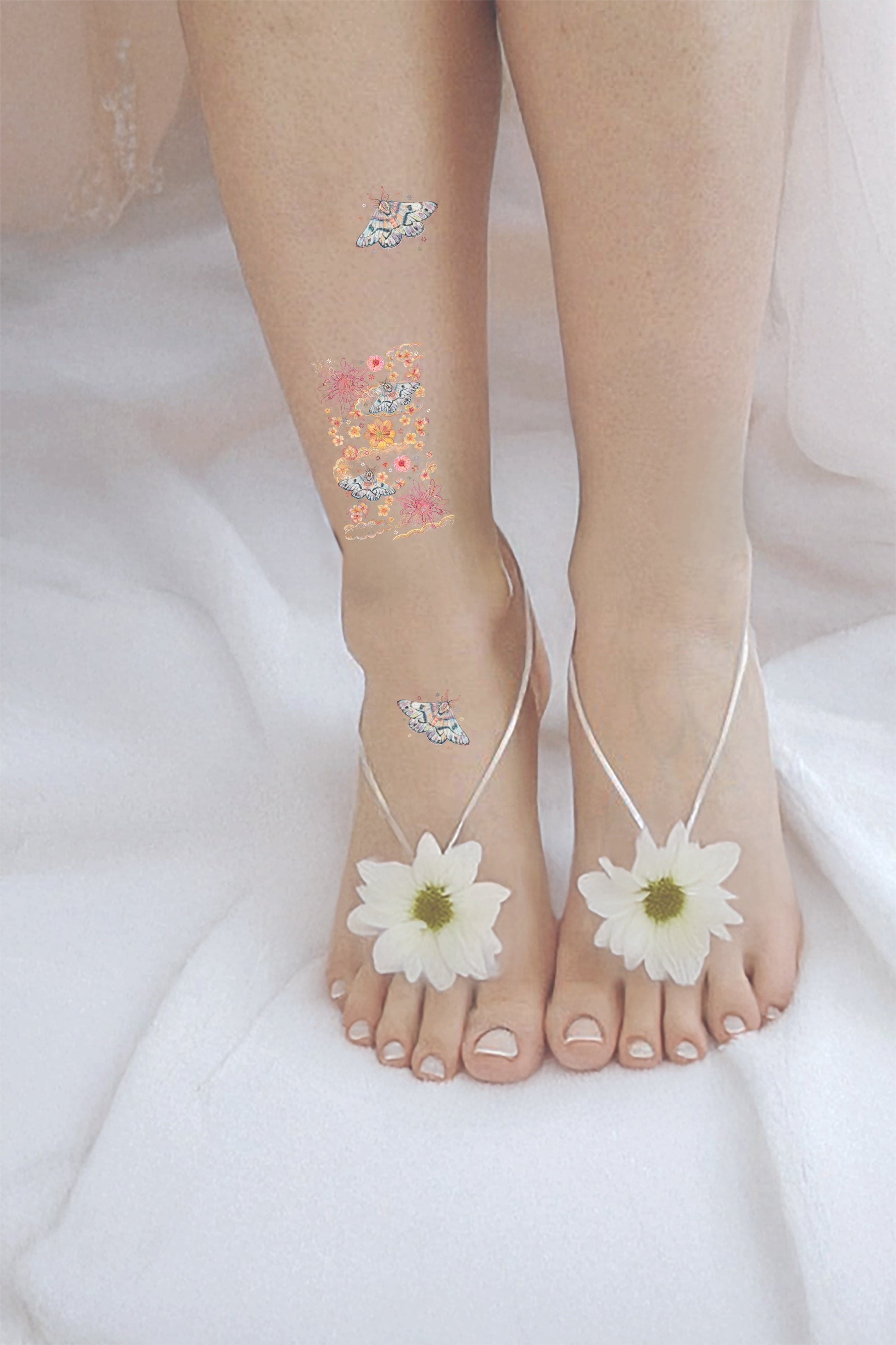 Bare feet with white sandals and floral anklets on a white background