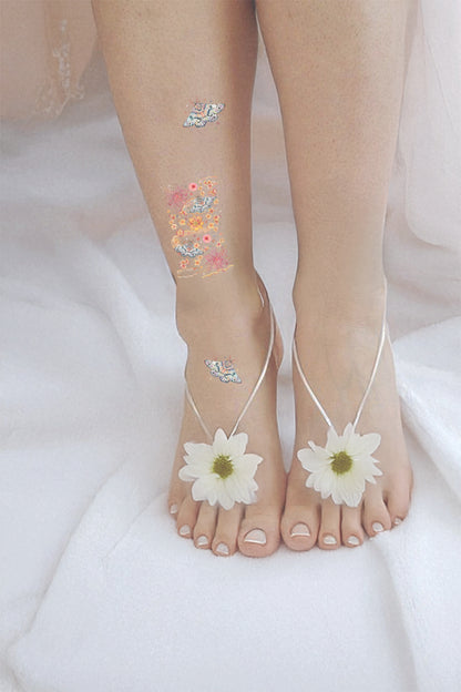 Bare feet with white sandals and floral anklets on a white background